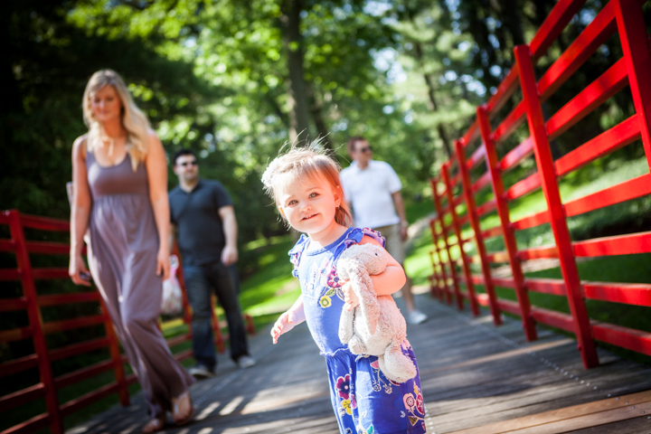 A child walks ahead of adults across a bridge with red railings.