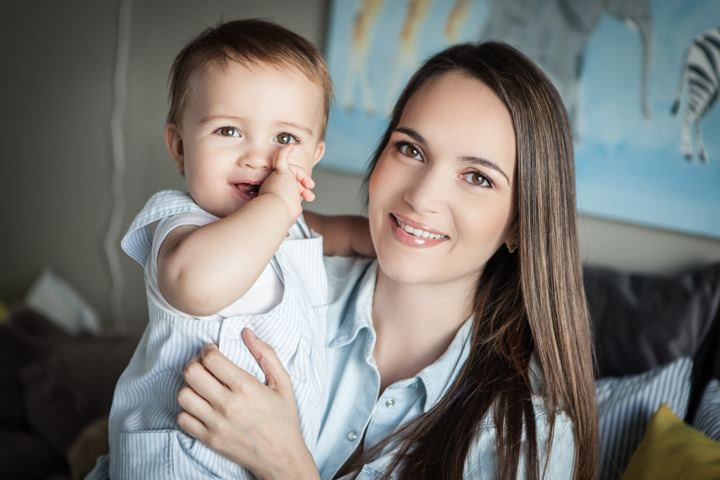 A smiling woman holds a baby close to her shoulder.