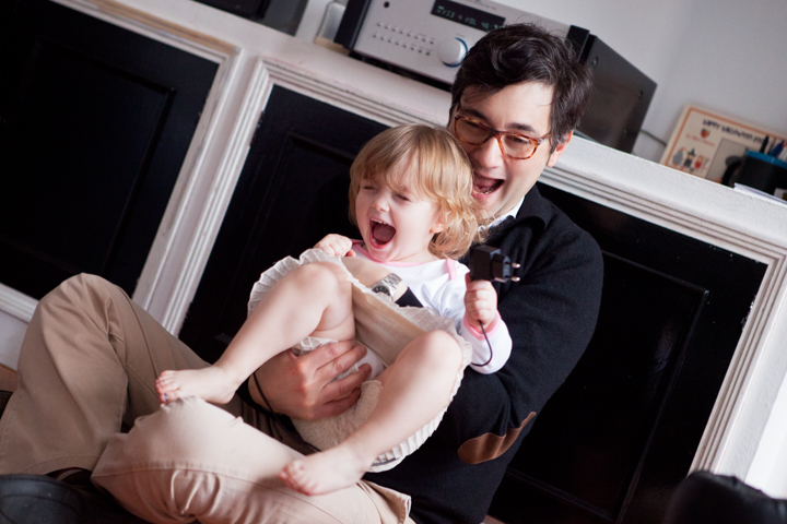 A smiling man holds a laughing toddler indoors.