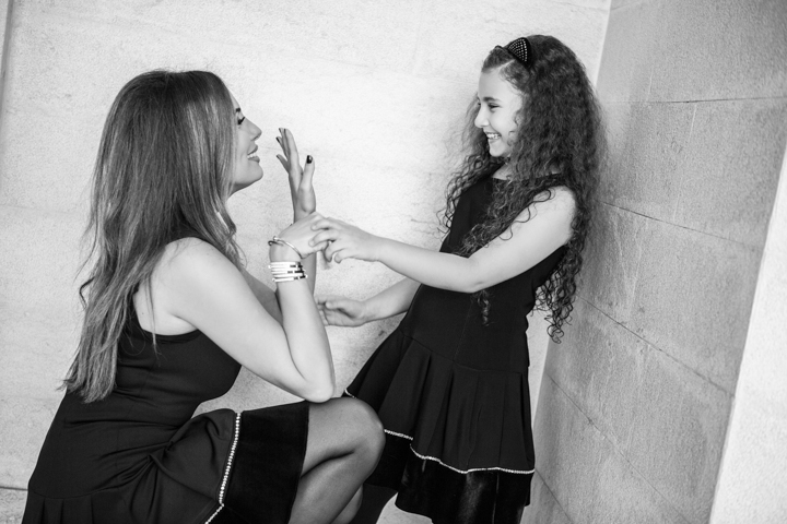 A woman and child touch hands beside a stone wall in black and white.