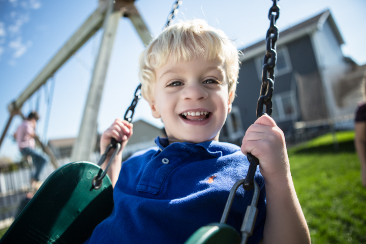 A laughing child holds the chains of a garden swing.