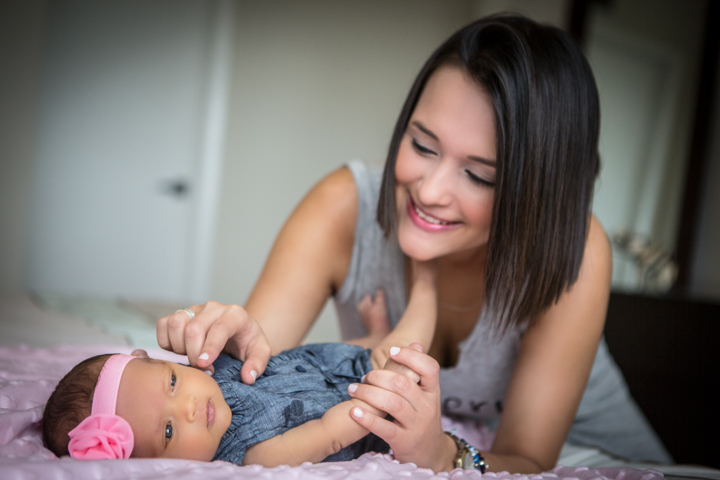 A woman gently adjusts a baby's clothing while the baby lies on a soft surface.