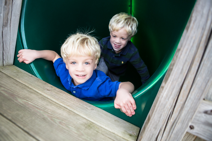 Two smiling children peek out of a green playground slide.