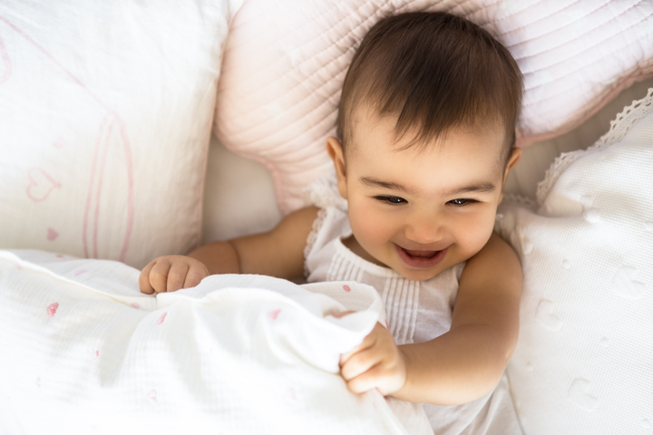 A smiling baby peeks from beneath a white duvet.