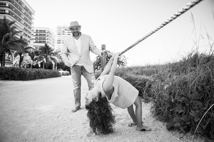 A child swings upside down from a rope while an adult watches in black and white.