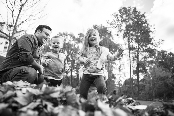 Two adults and two children play among fallen leaves in black and white.