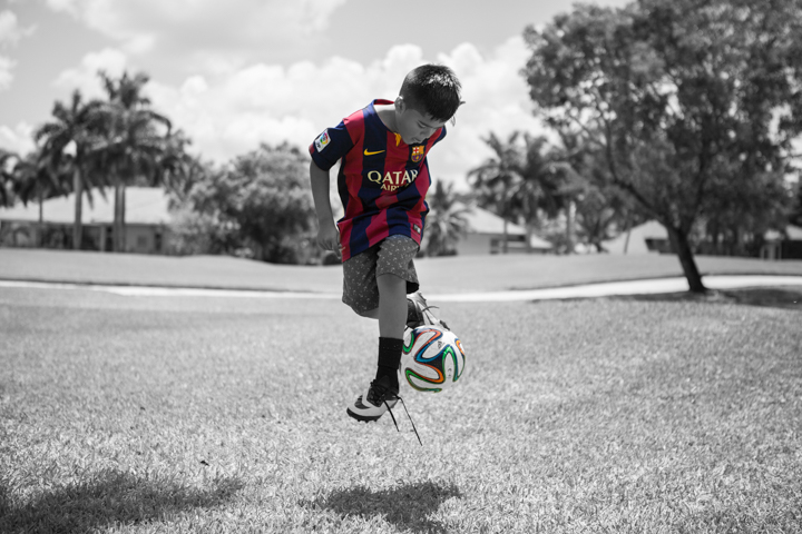 A child in a soccer kit jumps with a ball on a grassy field.