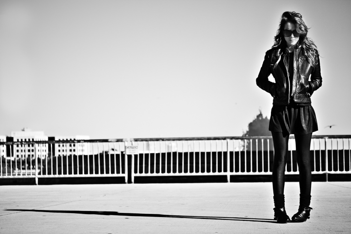 A woman in dark clothing stands beside a waterfront railing.