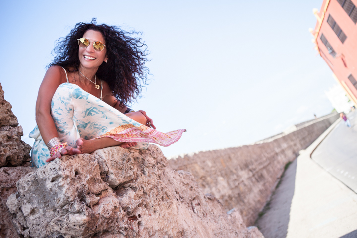 A woman sits on a stone wall beneath a clear blue sky.