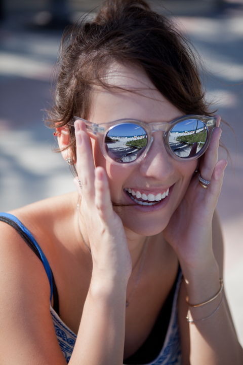 A smiling woman in mirrored sunglasses rests her hands beside her face.