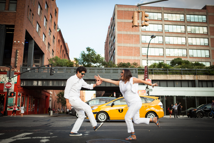 Two adults in white jump toward each other beside a yellow taxi.