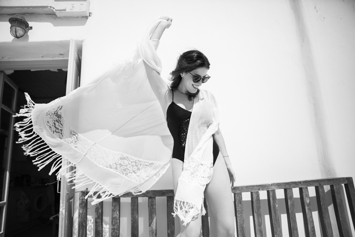 A woman spreads a fringed shawl beside a white building.