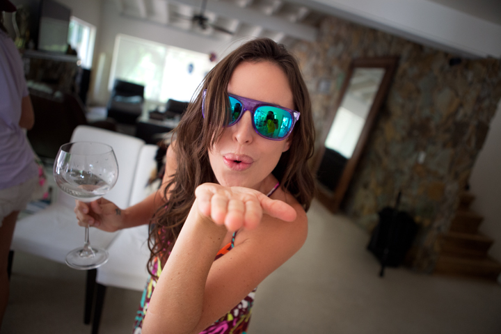 A woman wearing mirrored sunglasses holds a glass at a table indoors.