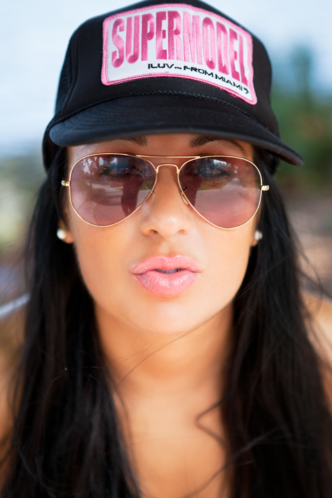 A woman wears aviator sunglasses and a black baseball cap.