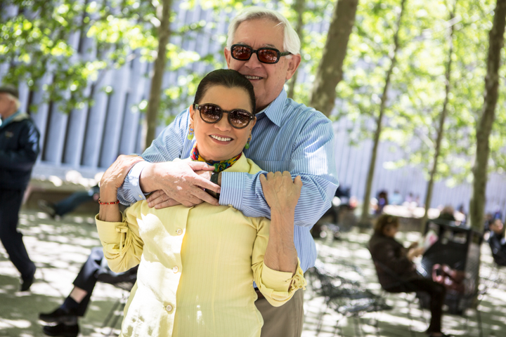 A man hugs a smiling woman from behind in a green park.