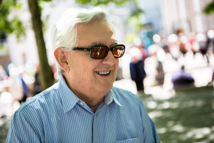 A smiling man in sunglasses and a striped shirt at an outdoor gathering.