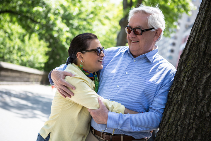 Two adults embrace beside a tree on a garden path.