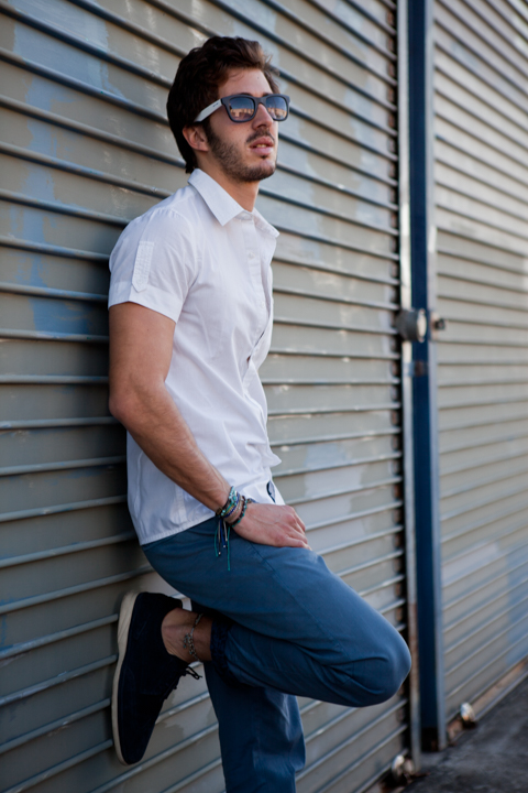 A man in sunglasses and a white shirt leans against metal shutters.
