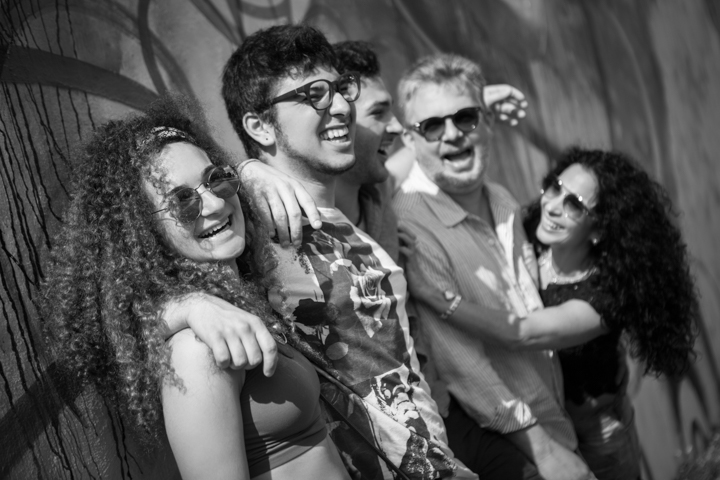 Four people lean together laughing in a black-and-white group portrait.