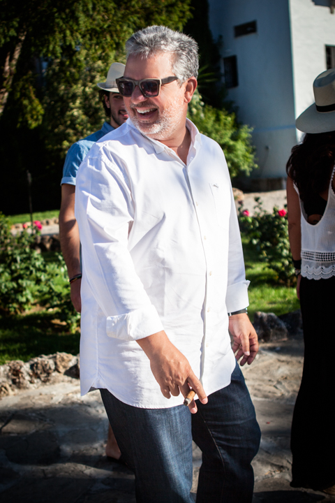A smiling man in a white shirt stands on a sunny garden path.