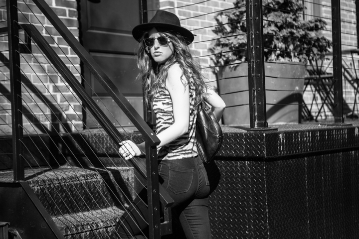 A woman in a hat and sunglasses stands beside an outdoor staircase.