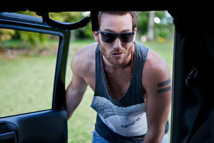 A man in sunglasses and a sleeveless top leans into an open vehicle.