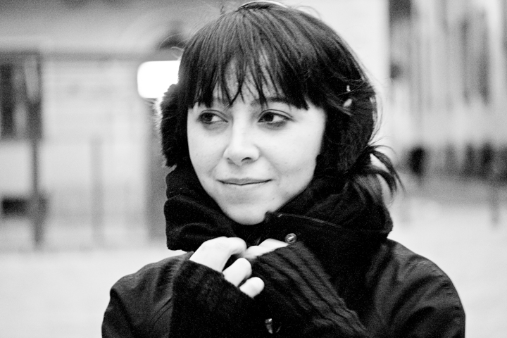 A woman in dark gloves and a scarf looks to one side.