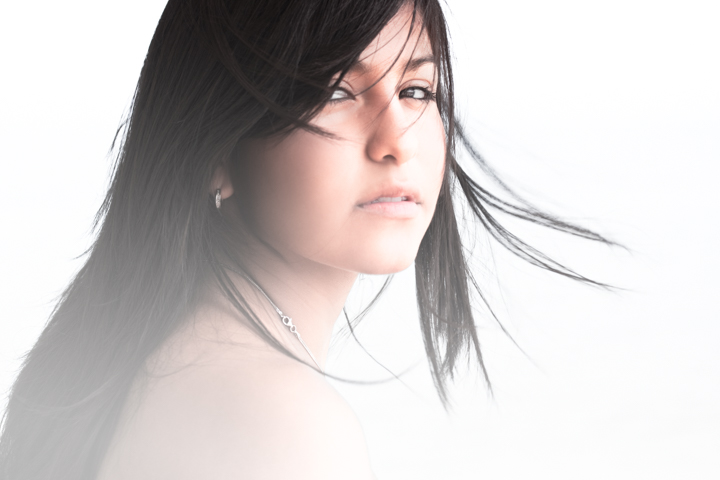 A woman with windblown dark hair photographed against a pale background.