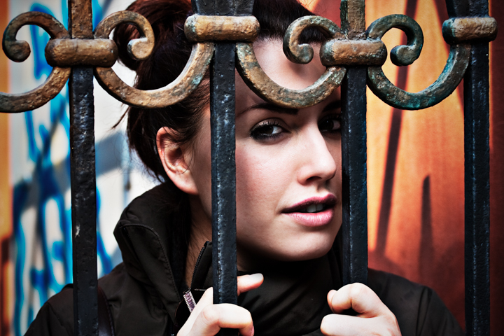 A woman holds the bars of an ornate metal gate.