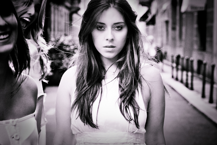 A woman with long hair walks along a narrow city street.