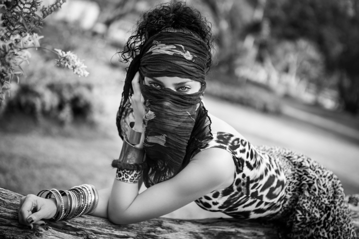 A woman reclining outdoors holds a patterned scarf across her face.