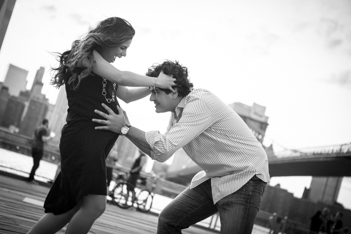 Two adults dance together on a waterfront walkway in black and white.