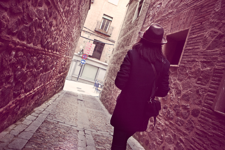 A woman in a dark coat walks through a narrow stone passage.