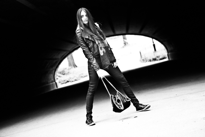 A woman carrying a handbag stands beneath an arched passage in black and white.