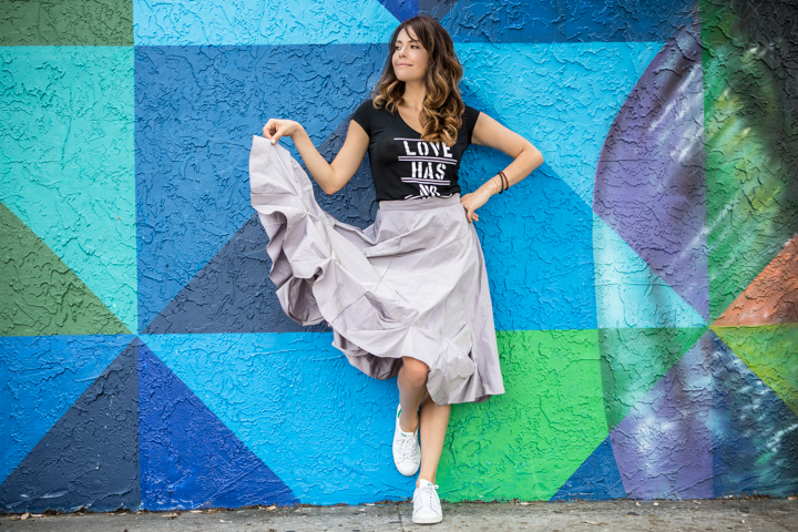 A woman holds out her skirt in front of a colorful geometric mural.