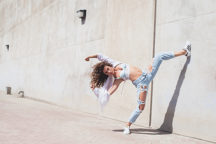 A person balances on one leg with the other raised against a sunlit wall.