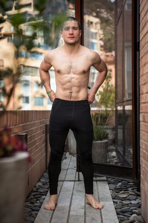 A shirtless man stands with his hands on his hips in an outdoor passageway.
