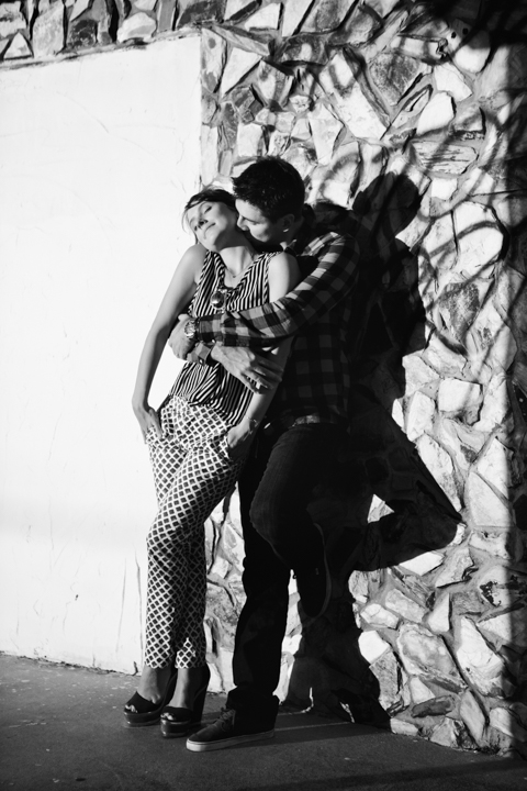 Two adults lean against a wall patterned with shadows in black and white.