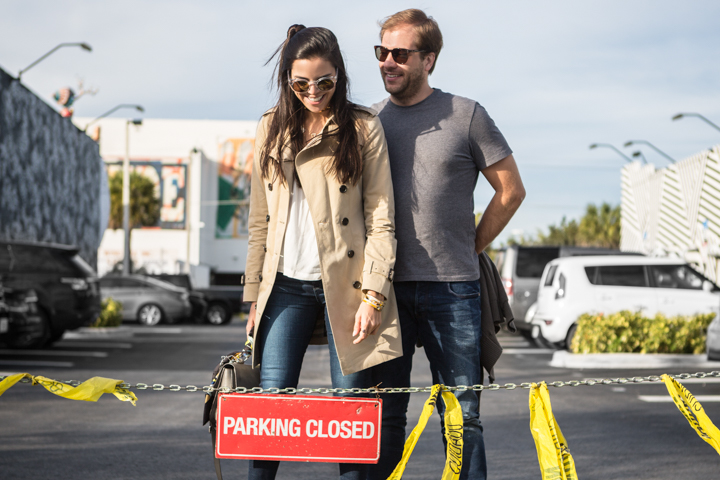Two adults stand together behind a parking barrier on a sunny street.