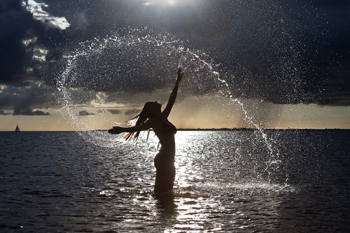 A person throws water into the air while standing in the sea at sunset.