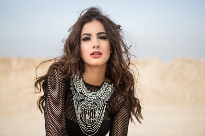 A woman wears layered silver necklaces and black mesh sleeves outdoors.
