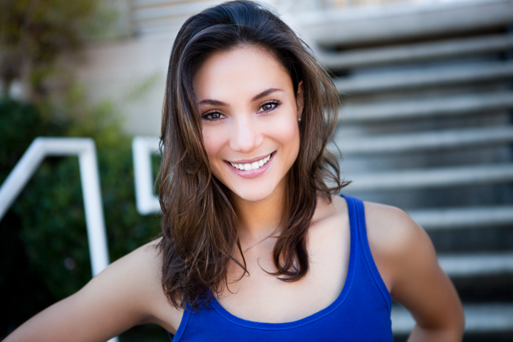 A smiling woman in a blue sleeveless top sits on garden steps.