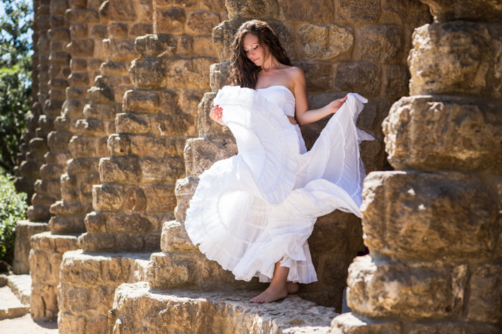 A woman spreads her flowing white skirt inside a weathered stone arch.
