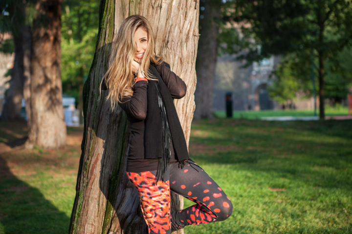 A woman leans against a tree with one leg bent in a green park.