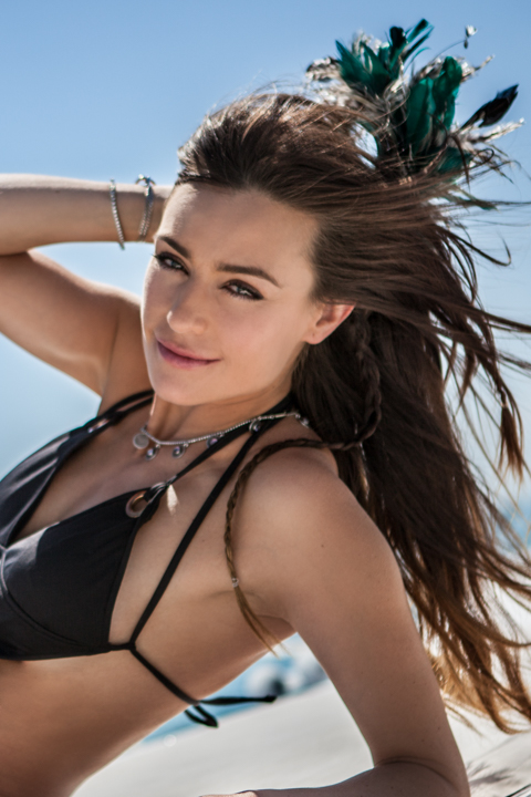 A woman in a black bikini lifts a hand behind her head in bright sunlight.