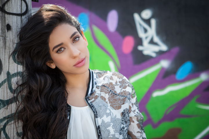 A woman in a patterned jacket stands beside a colorful graffiti mural.