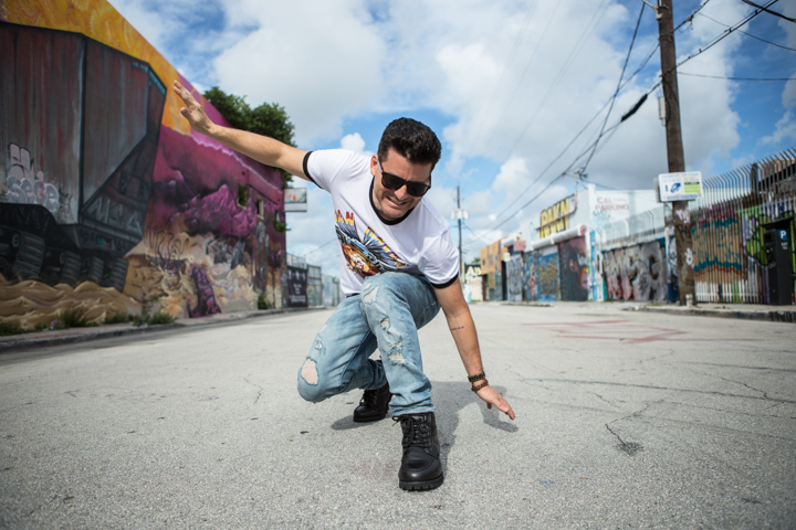 A man in sunglasses jumps beside a street mural with one arm outstretched.
