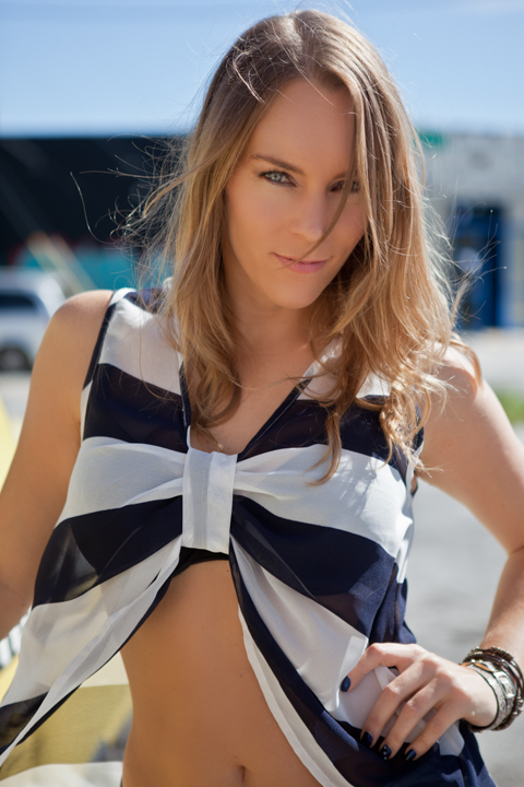 A woman in a striped crop top stands by the sea.