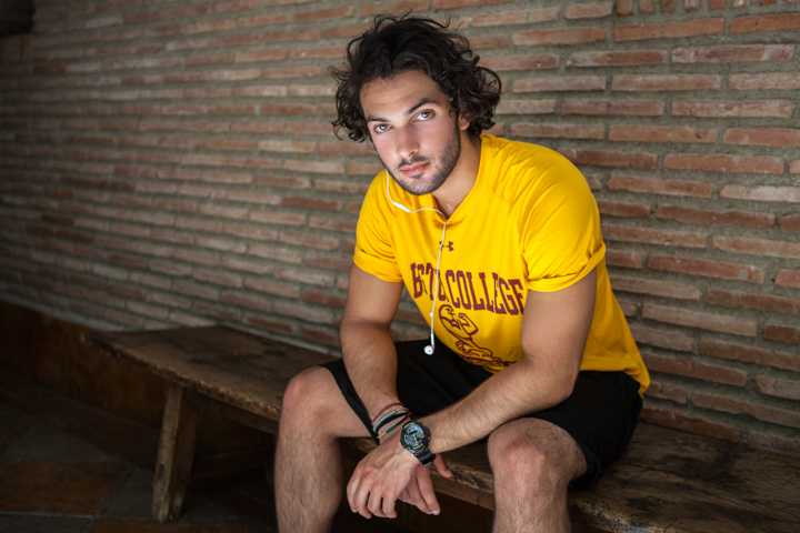 A man in a yellow T-shirt sits on a bench against a brick wall.
