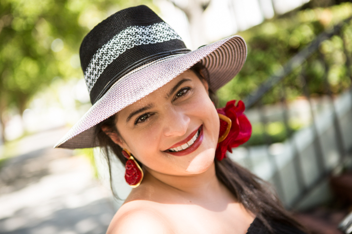 A smiling woman wears a pink and black hat with red statement earrings.